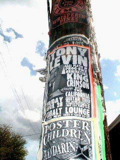 A telephone pole serves as an advertising platform for a CGT/Tony Levin poster.
