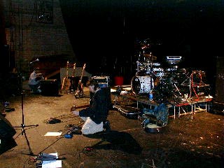 The stage is dark and nearly empty except for Paul, and Pat's drum kit.